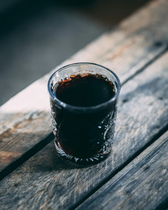 a glass filled with dark liquid sits on a wooden bench