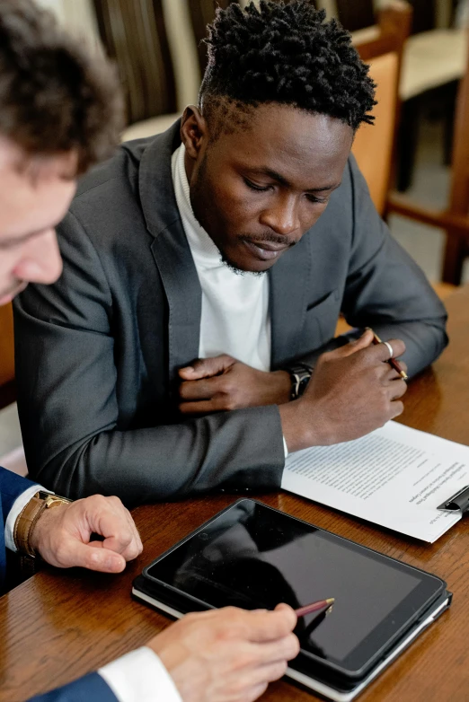 two men sitting at a table working on a tablet