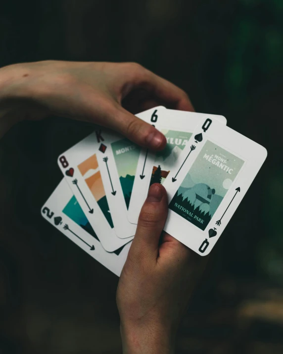 four hands holding four different playing cards, with a hand holding another deck