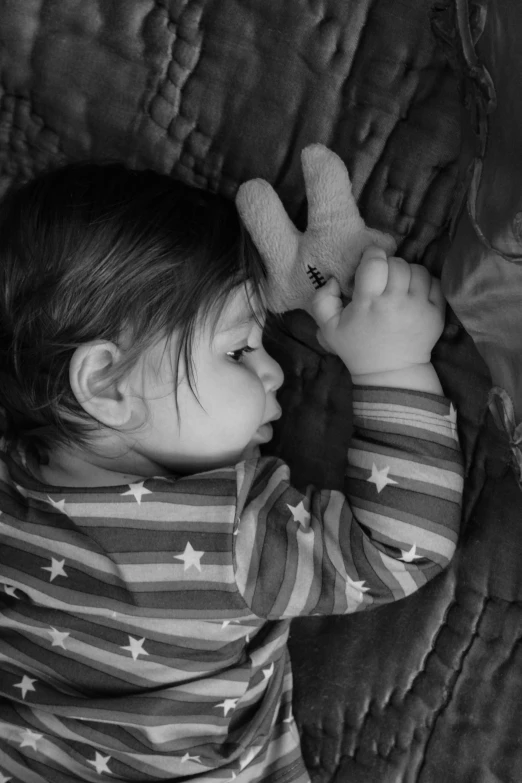 a small girl laying on the bed while holding a toy