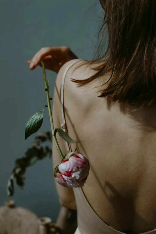 a woman is holding a red rose with green stems