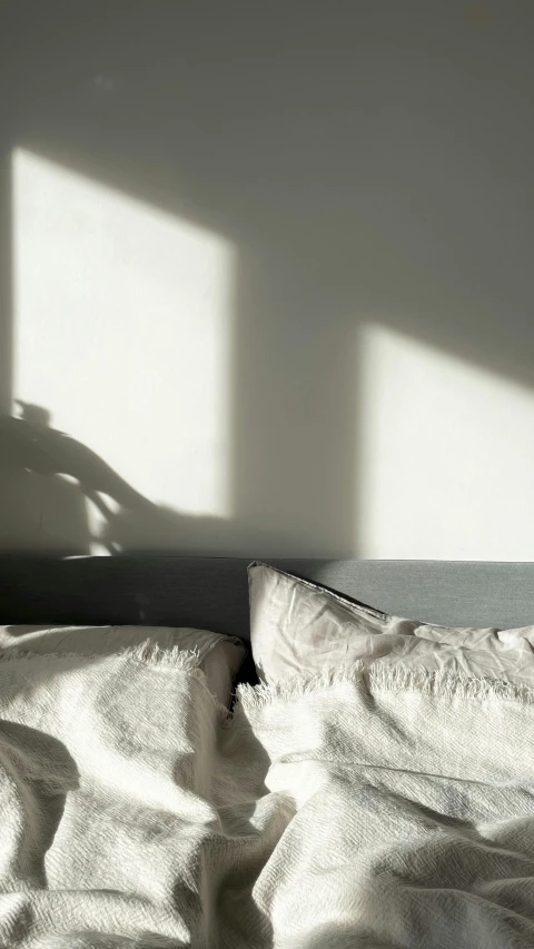an unmade bed with two shadows of lamps on the wall