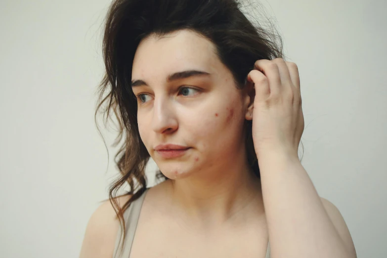 a woman with dark brown hair holding her hand against her head