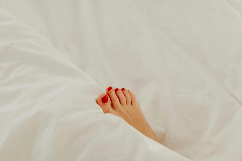 a woman with red nails laying in white sheets