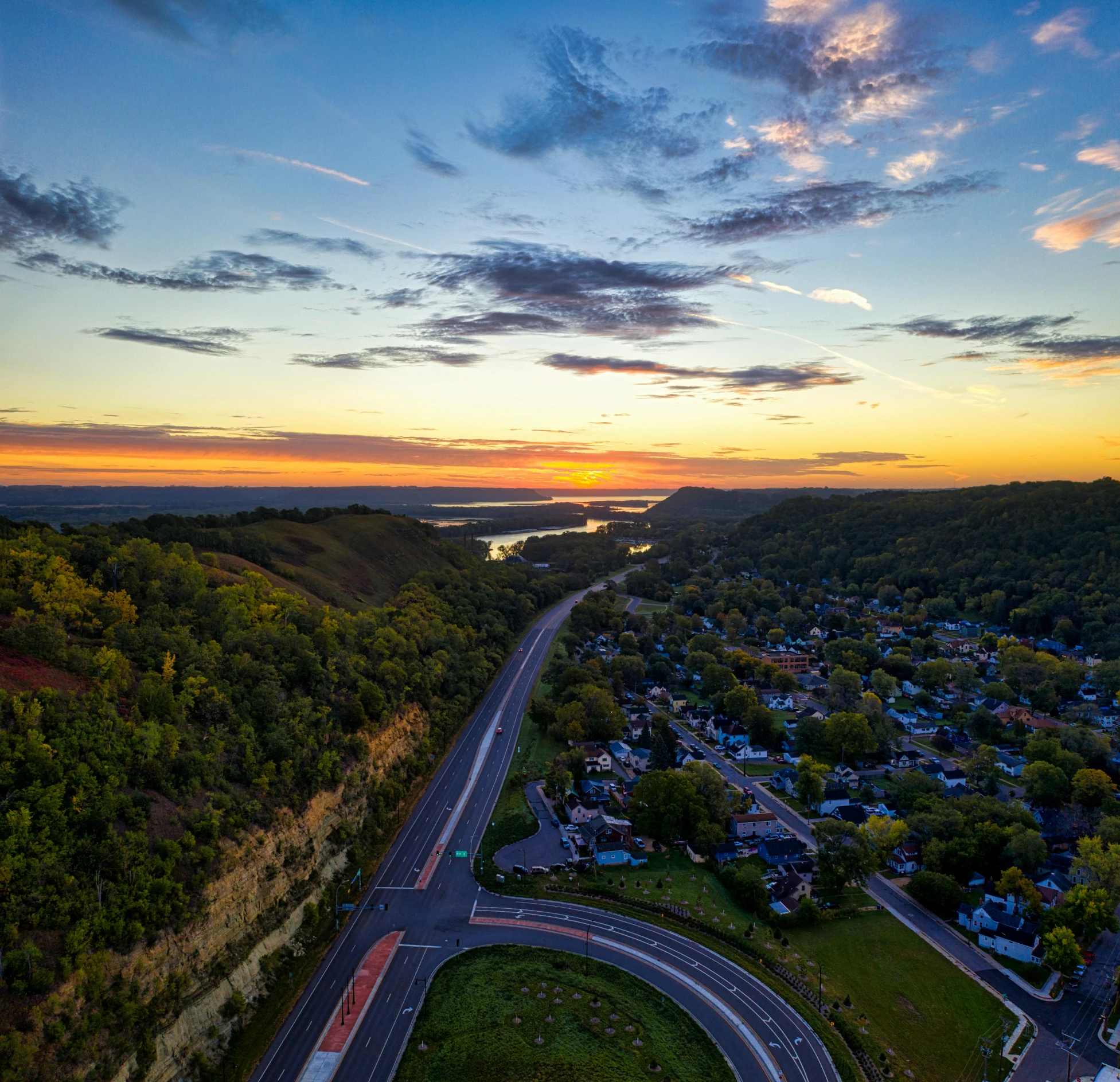 an aerial view of a highway near some trees and a body of water