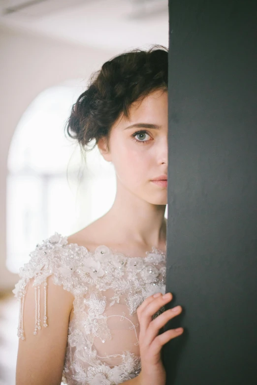 the bride poses behind a wall in her white dress