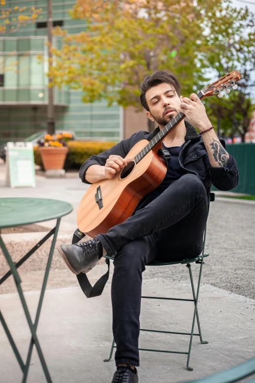 a man sitting down playing a guitar while talking on a cell phone