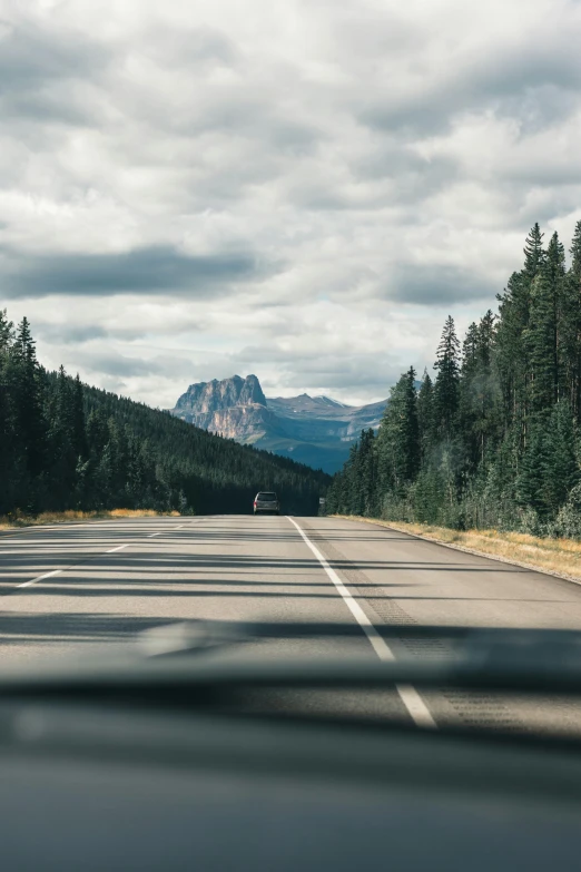 a car driving down a country road, with mountains in the background