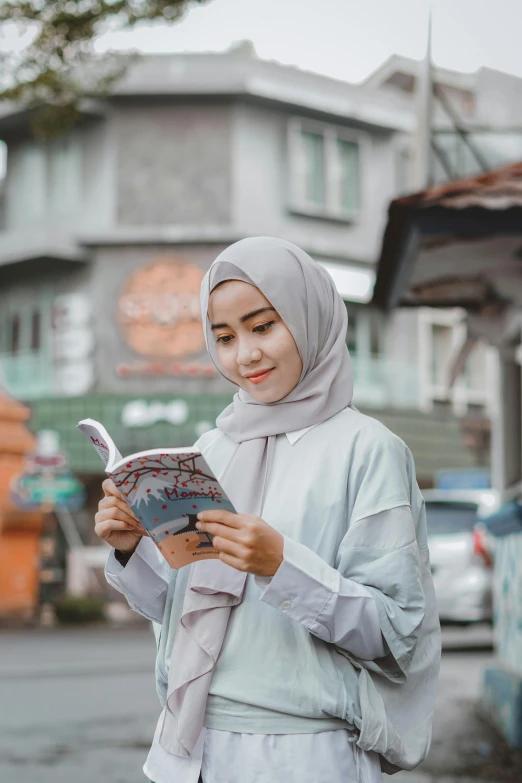 an asian woman standing outside of a building looking at a book