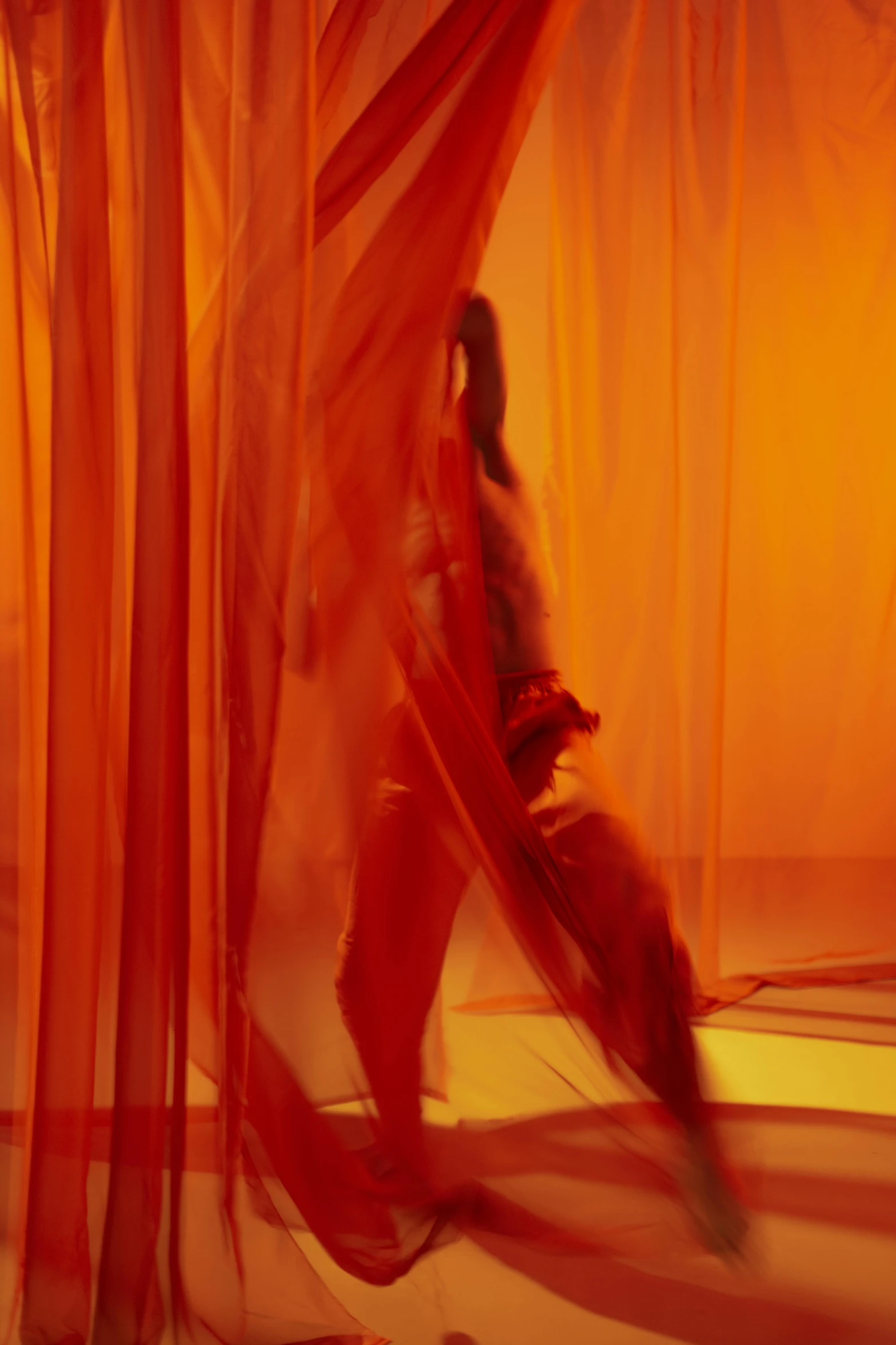 a person walking behind a red curtain with long orange material