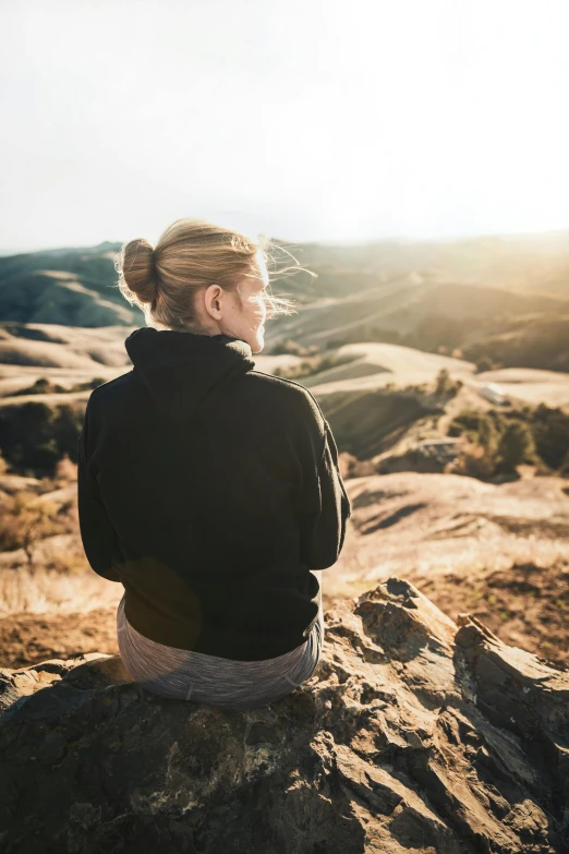 the girl is sitting on a rock looking at soing in the distance