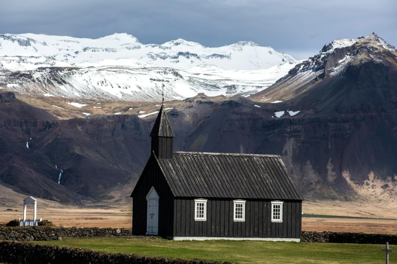 a little house with a black roof and snow capped mountains in the background