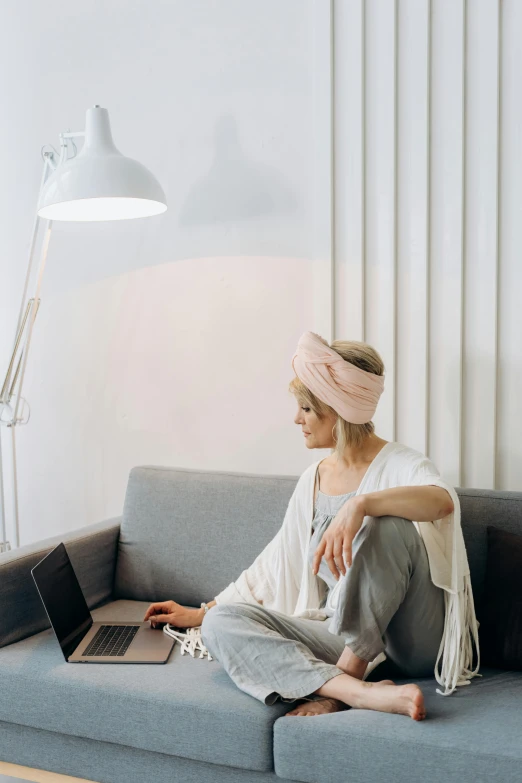 woman sitting on couch in white room with laptop and pink scarf