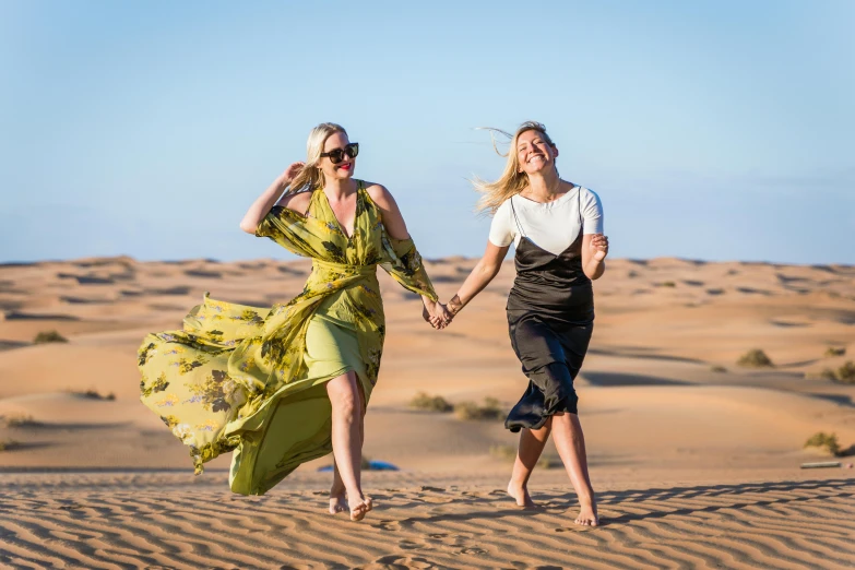 two women walking across sand dunes together