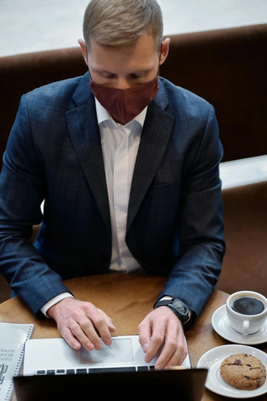 a man wearing a face mask sitting in front of his laptop