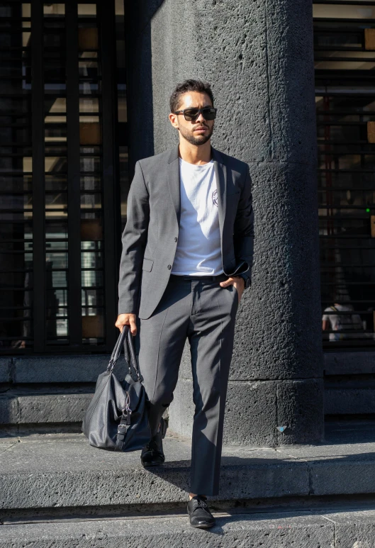 man in grey suit with hand bag standing on a sidewalk