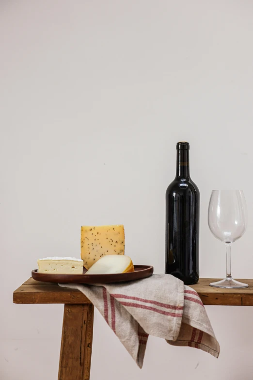 a plate of cheese, a bottle of wine and a glass on a table