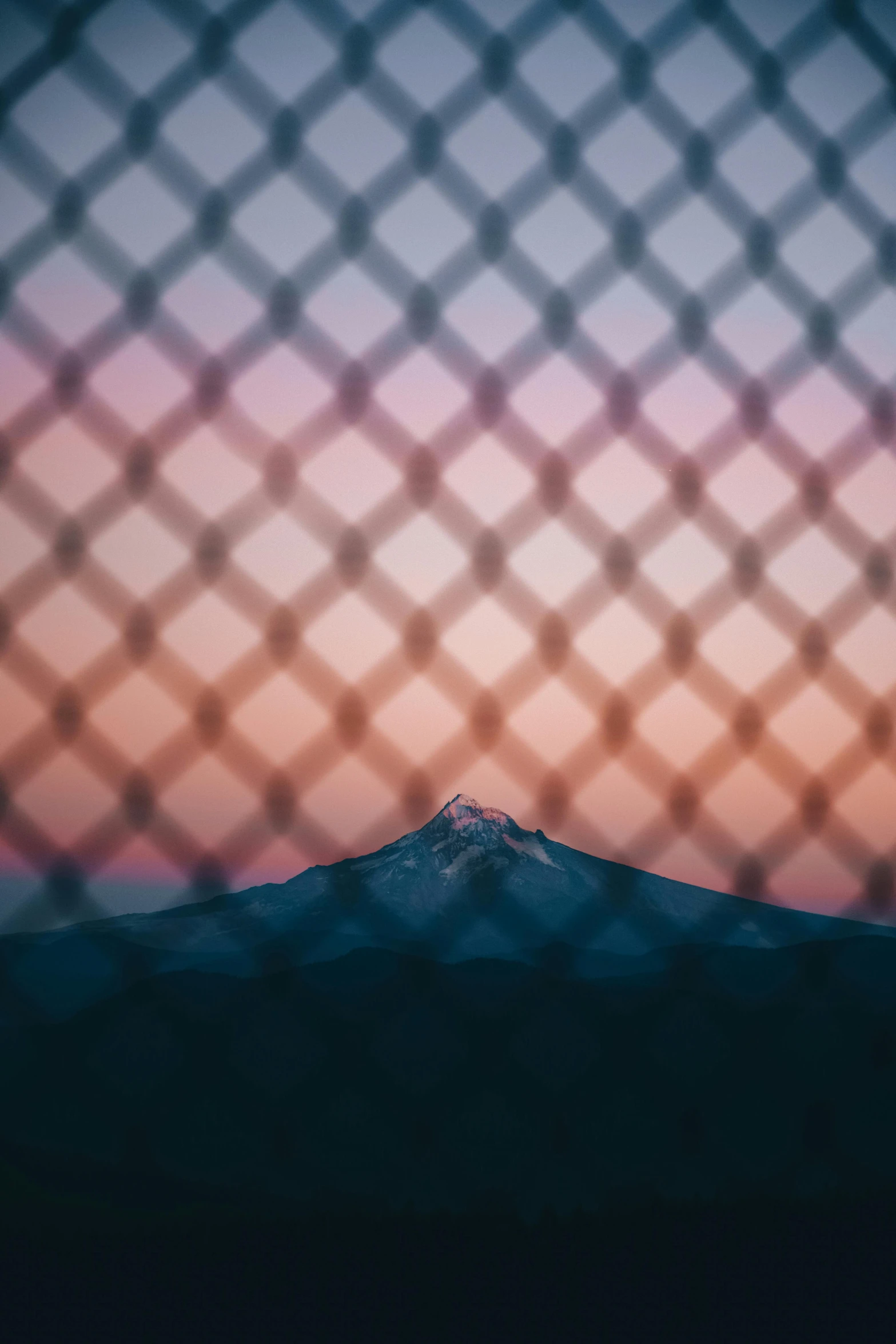 the sunset view of the mountain through an abstract mesh fence