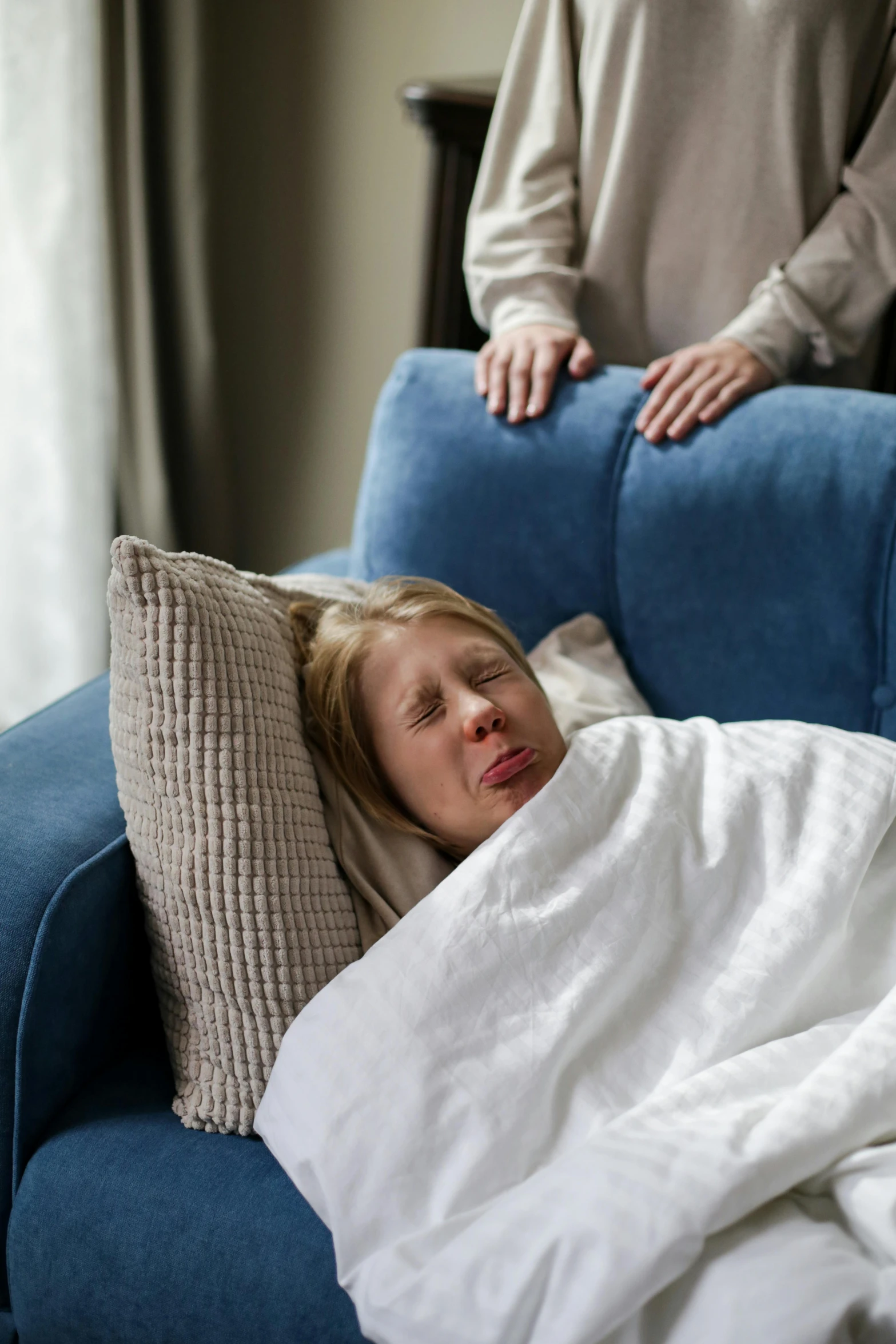 a woman sitting on a blue couch with white sheets