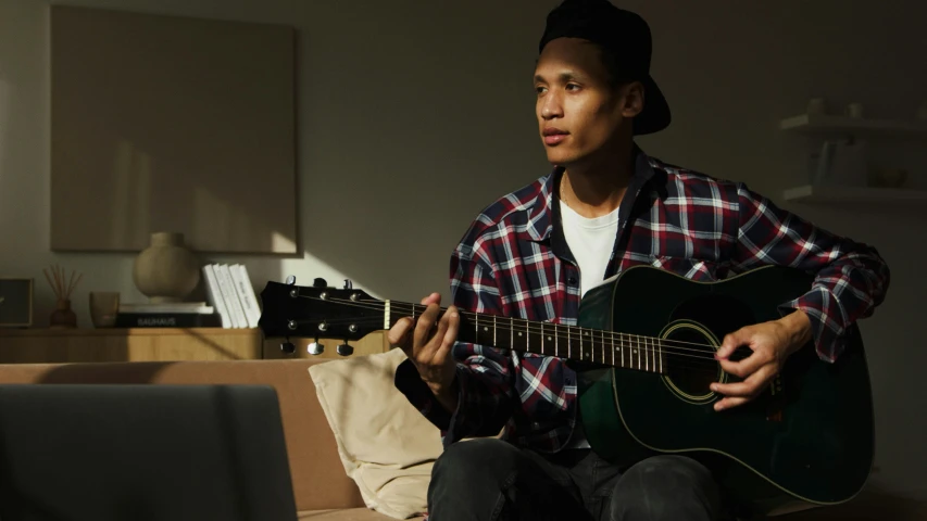 a man holding an acoustic guitar in front of his laptop