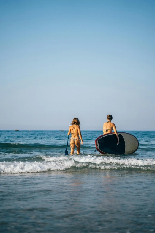 two people walk along the beach with their surfboards