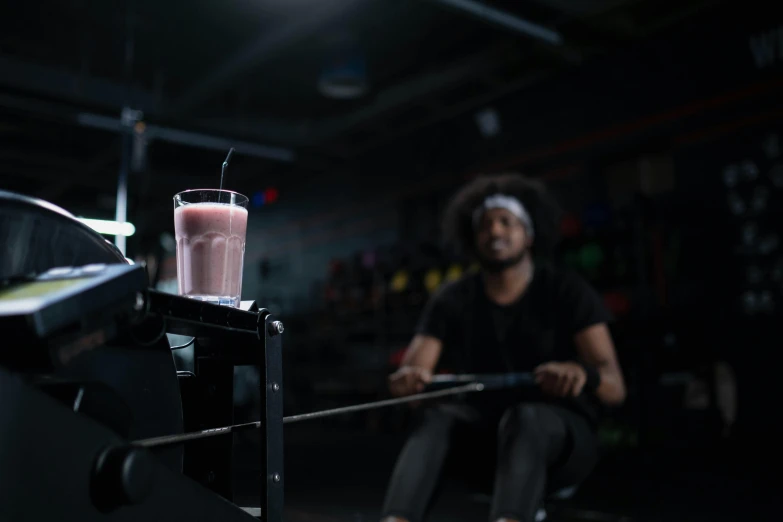 a guy holds onto some sort of machine as he sits next to a small glass with a liquid on it