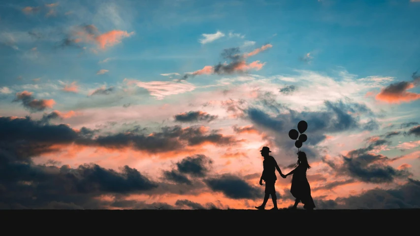 two people holding onto balloons and walking towards sunset