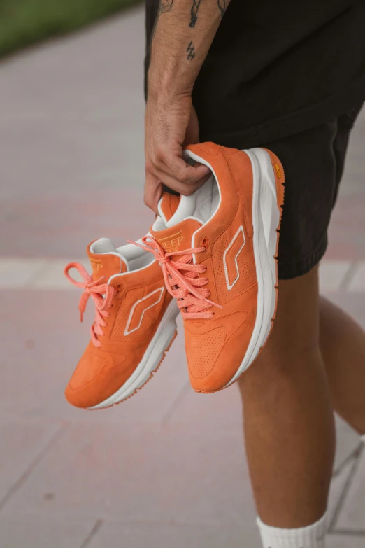 a person holding up a pair of orange sneakers