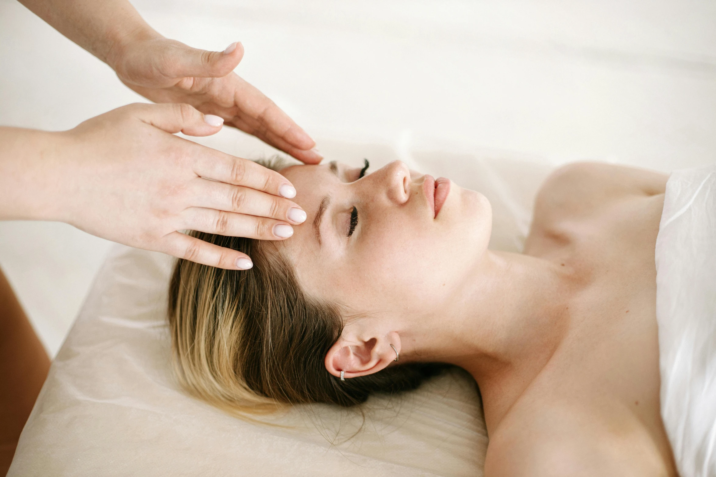 a woman laying down on top of a bed while having a head massage