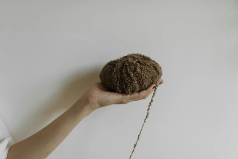 a person holds up a ball of yarn on the tip of a string