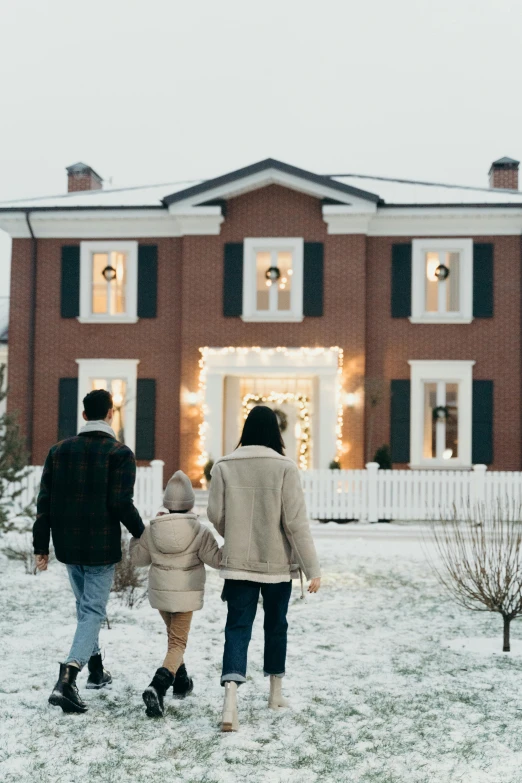 an adult and child are walking toward a red house