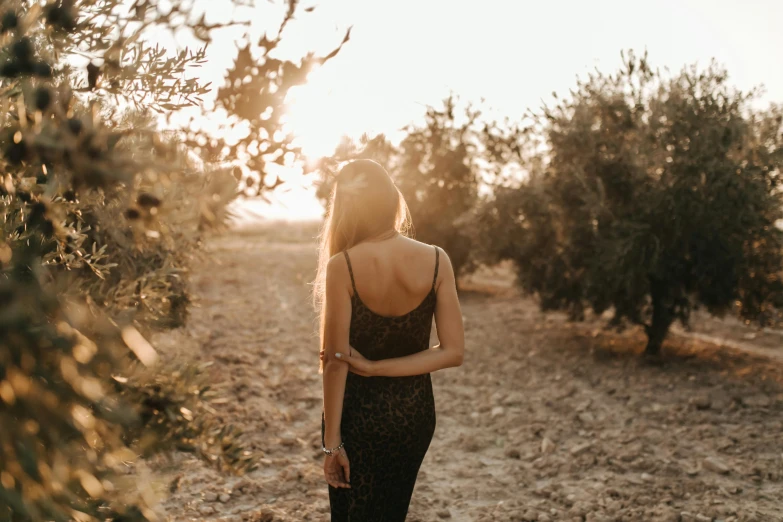 a woman in a dress standing under an olive tree