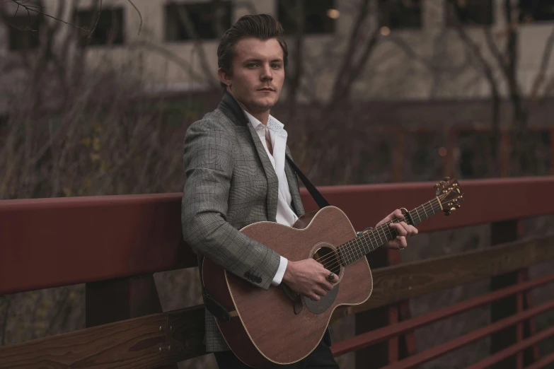 a man holding a guitar next to a wooden fence