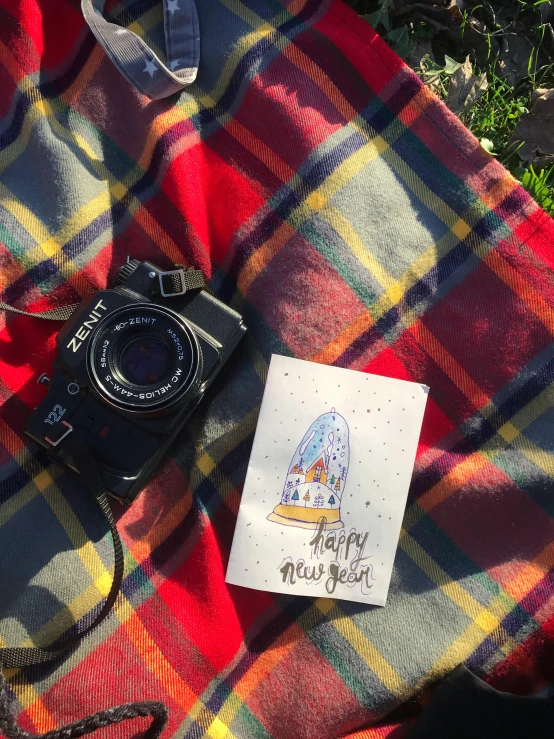 the camera is sitting on the blanket and next to the paper