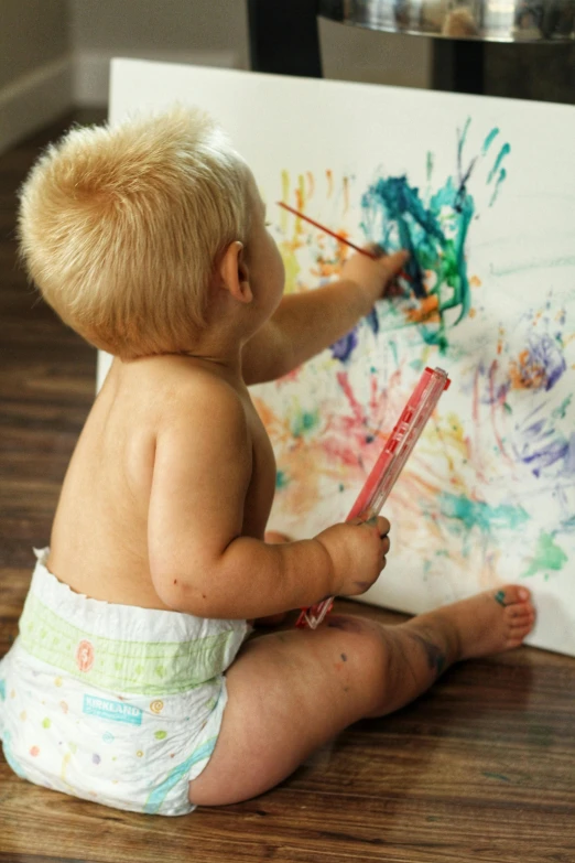 baby sitting on floor painting on canvas with crayons