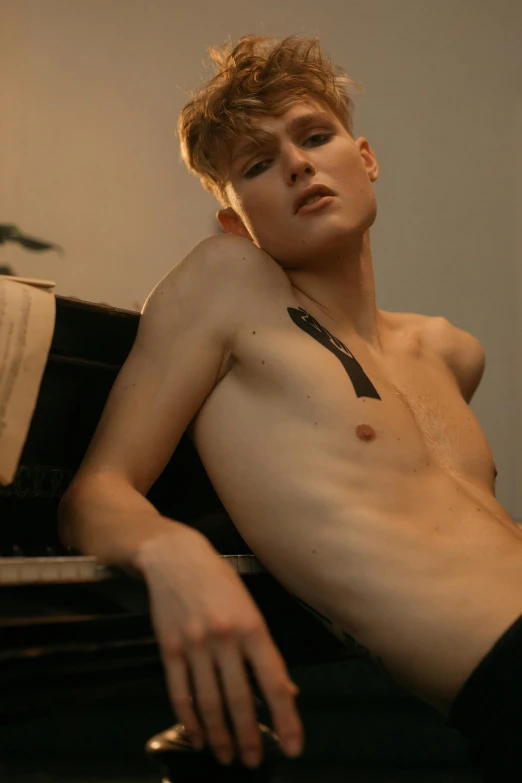 a young man with a short torso leans on a piano