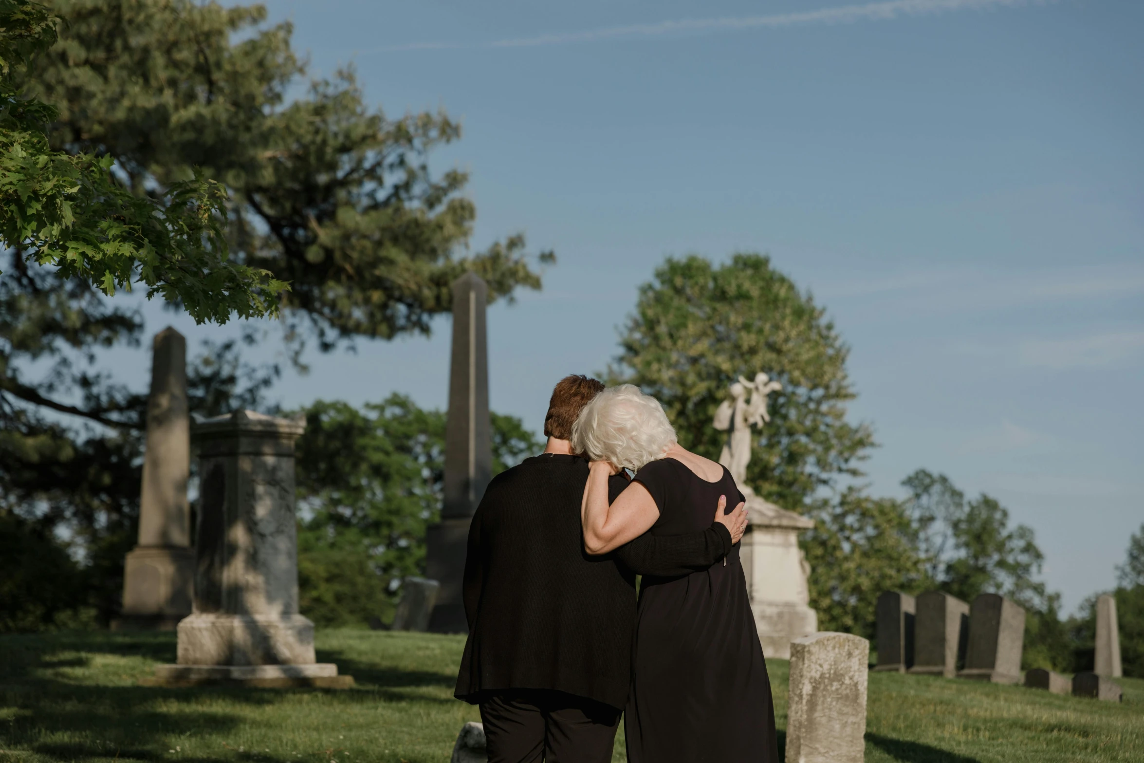 the elderly couple are hugging by a cemetery