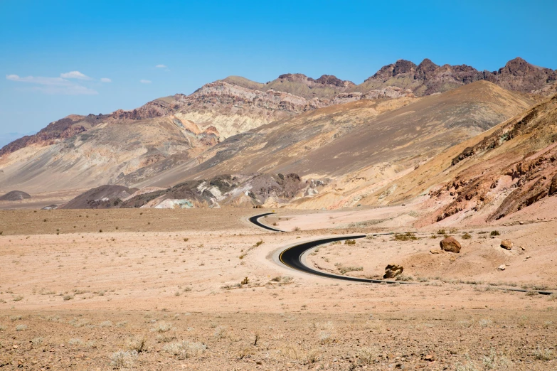 a wide winding road passing through mountains with a blue sky