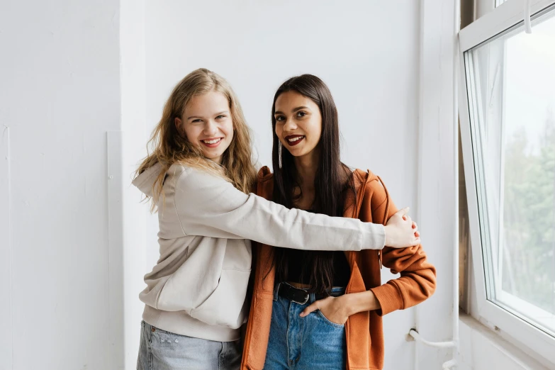 two pretty girls pose together in front of a window