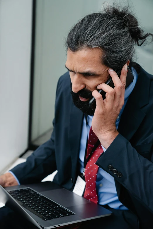 man wearing suit and tie sitting in front of laptop talking on phone