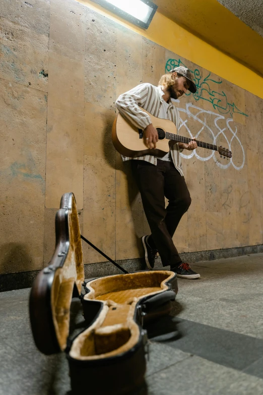 a young man leaning against a wall playing the guitar