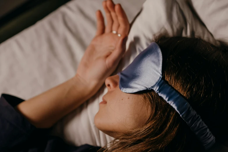 a woman laying in bed with her eyes closed wearing blindfold