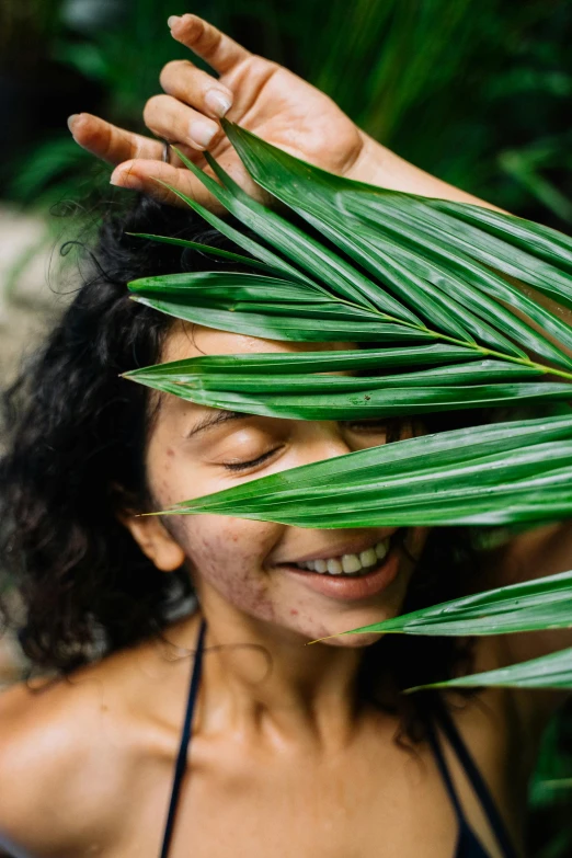 the woman smiles with her hand over her face behind leaves