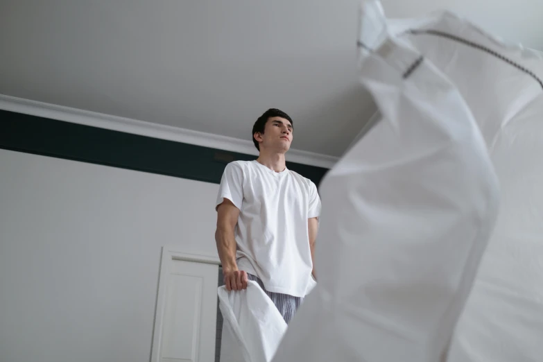 a young man is standing in the corner of his room with white sheets folded around him