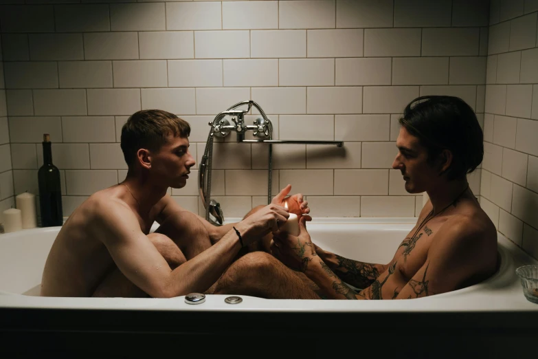 two people sitting in a bath tub while one man holds up an orange piece