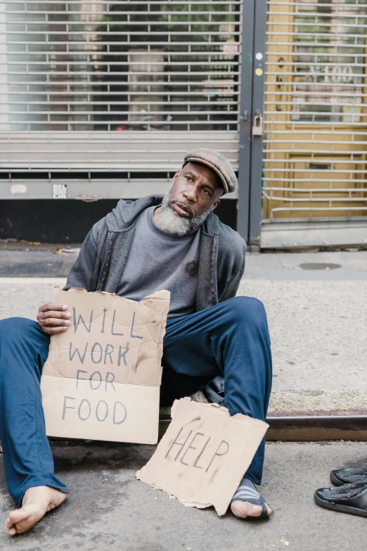 man sitting on the curb holding signs that say i will work for food