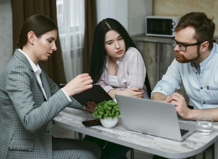 three people are sitting at a table looking at an open laptop computer