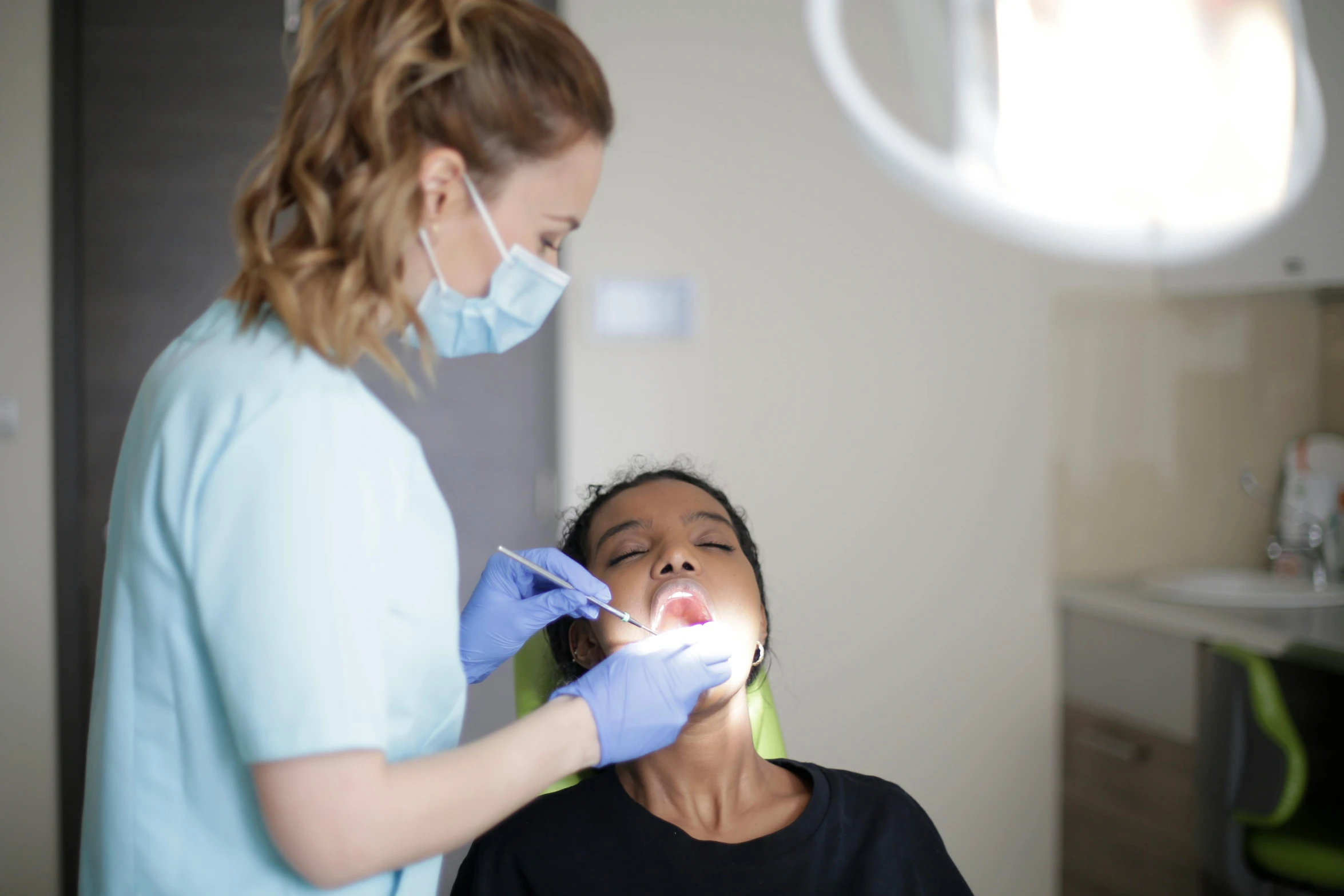 the young lady is having a procedure performed by the dentist