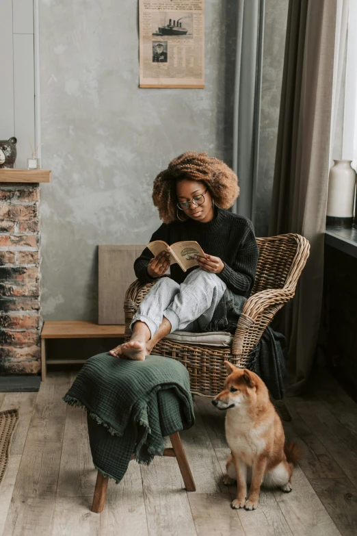 woman sitting in wicker chair with dog, looking at book