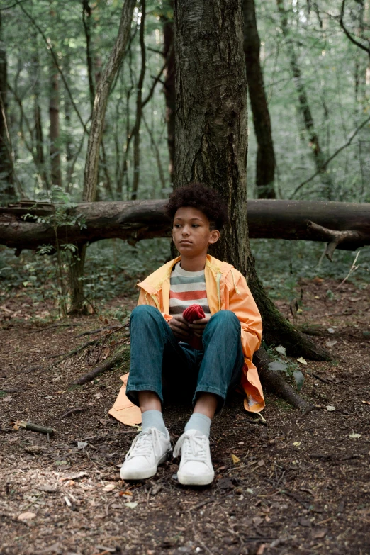 a small boy sitting under a tree in a forest